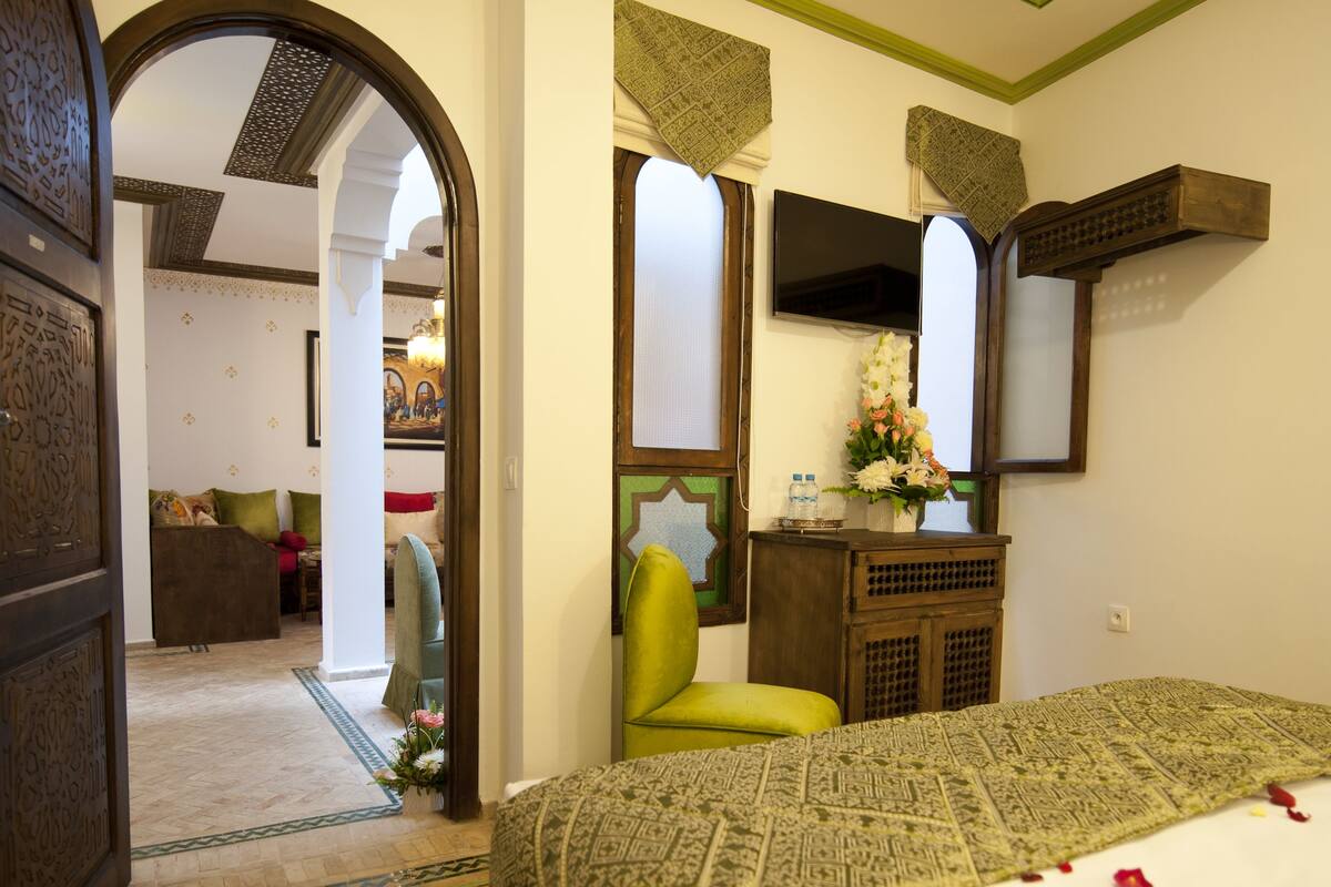 Una habitación de hotel con una cama, un sillón verde, un armario de madera y un espejo.