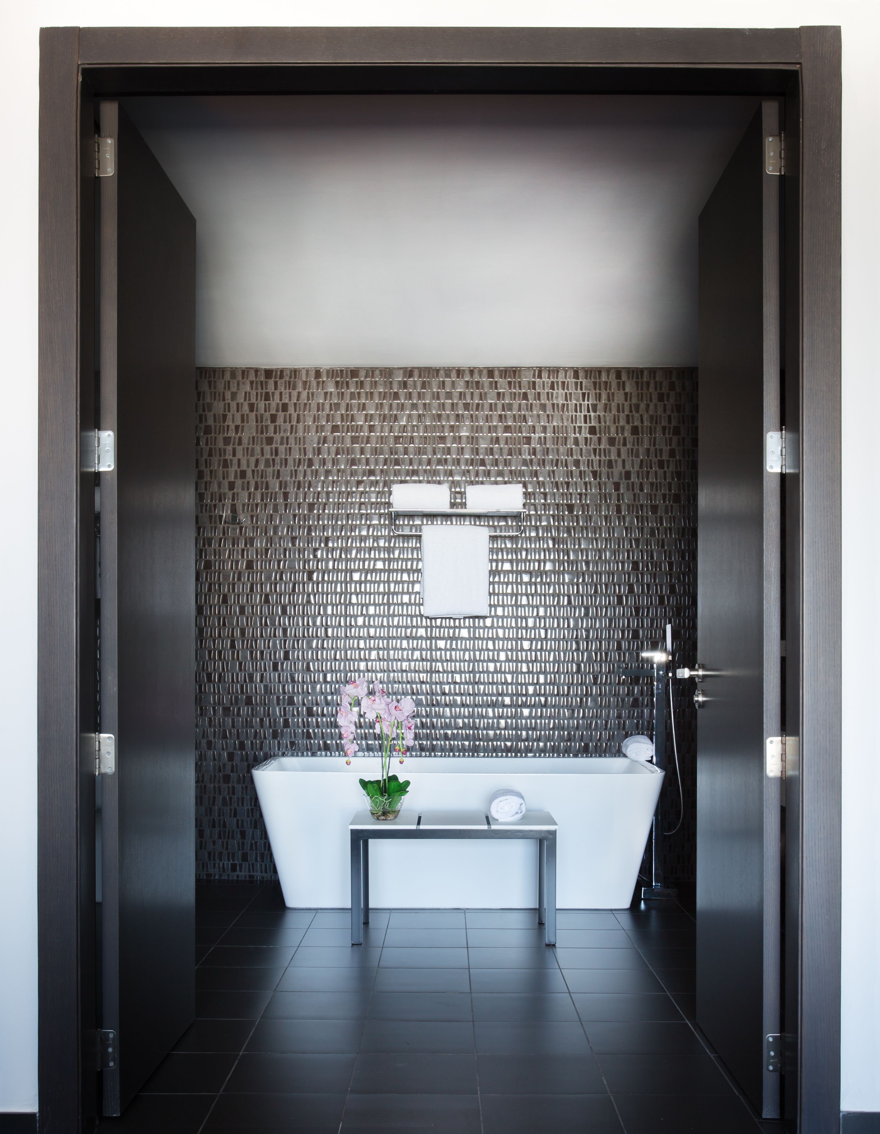 A modern bathroom with a freestanding bathtub, a small table with a vase of flowers, and a wall-mounted towel rack.