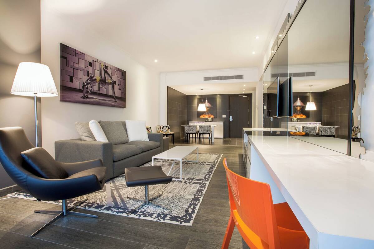 A modern living room with a sofa, a chair, a coffee table, and a dining area in the background.