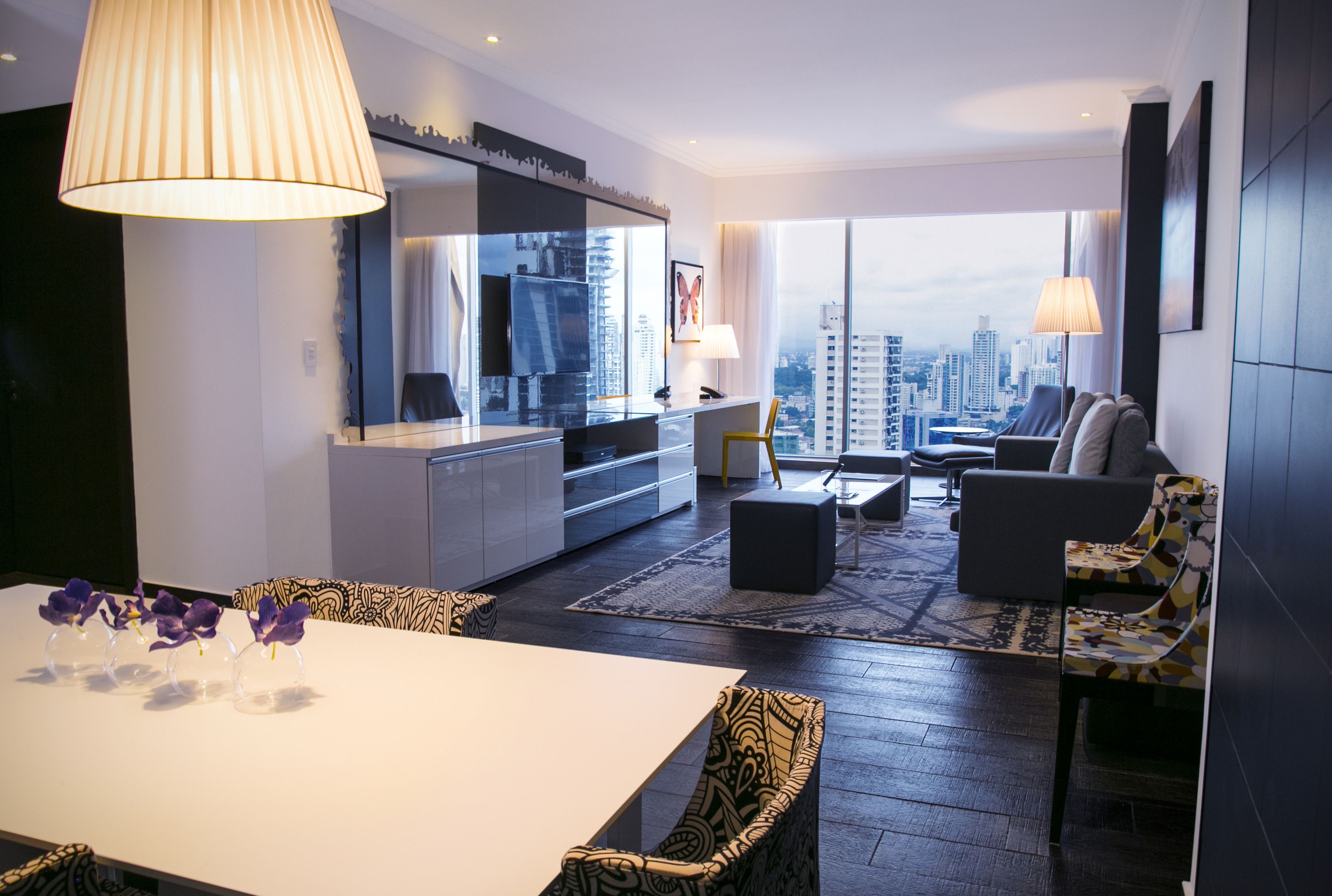 A modern living room with a dining area, a sofa, and a view of the cityscape.