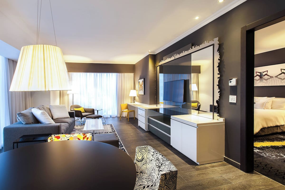 A modern hotel room with a sofa, dining table, and a large mirror.