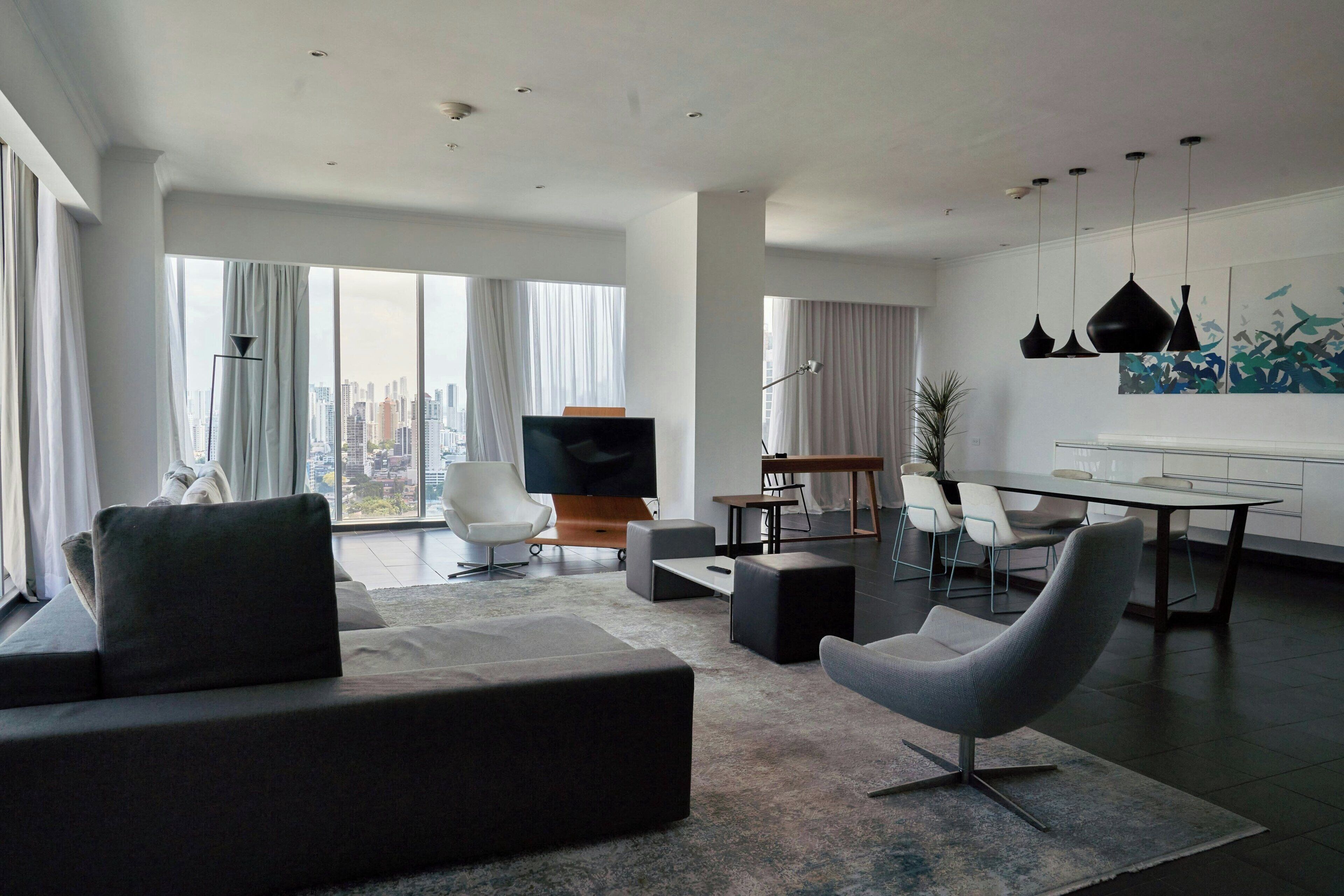 A modern living room with a large sofa, a dining table, and a flat-screen TV.