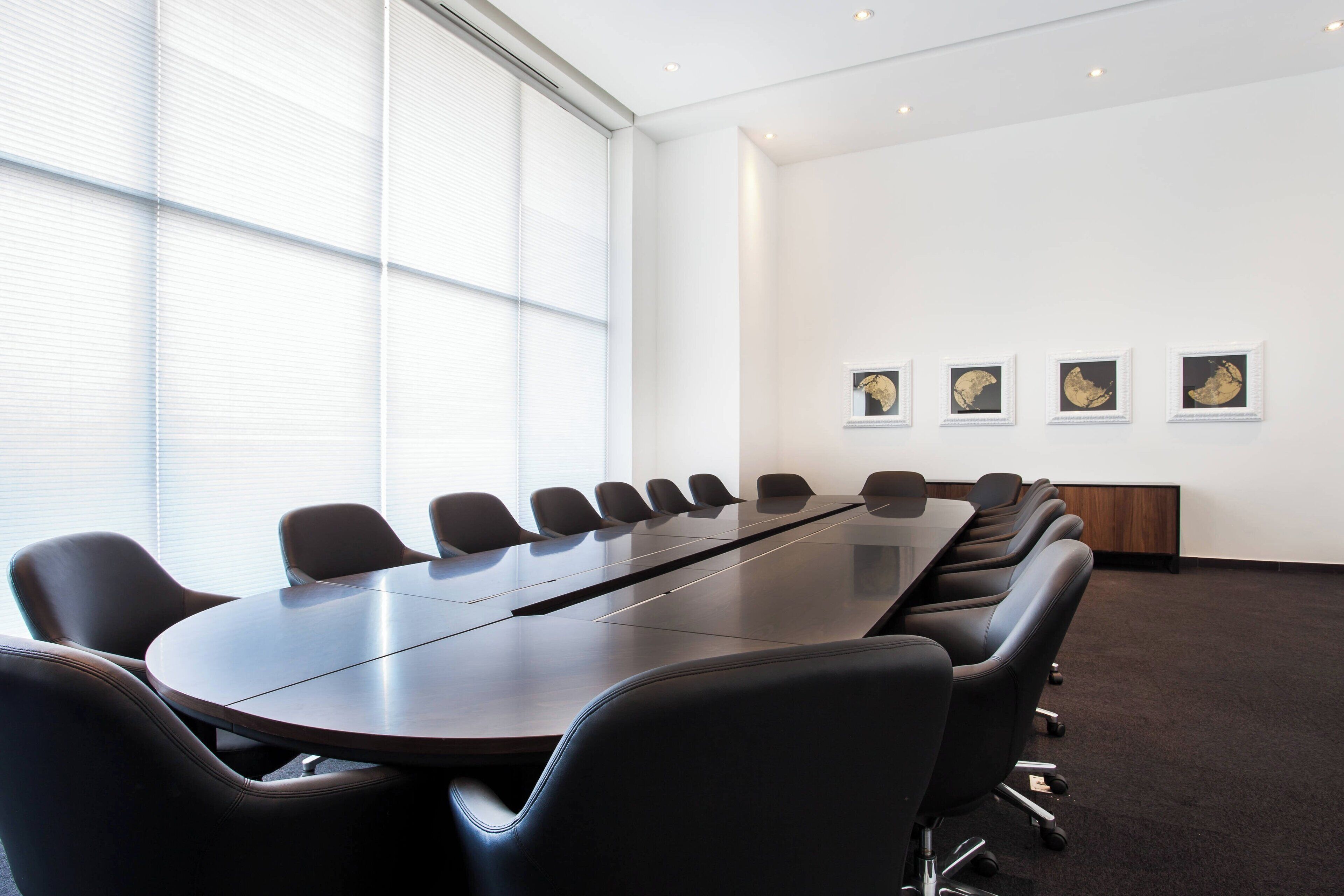 Un salón de conferencias con una larga mesa y sillas, ventanas grandes y cuadros en la pared.