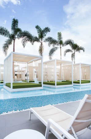 Un espace aménagé au bord de la piscine, avec des sièges couverts et des palmiers.