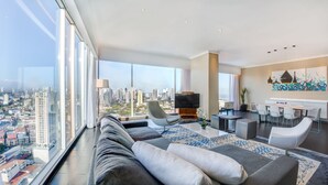 A modern living room with a city view, a flat-screen TV, and a dining area with white chairs and a table. - Sortis Hotel, Spa & Casino, Autograph Collection by Marriott (Panama City)