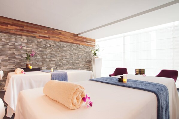 Une salle de spa avec deux lits, un mur en pierre et une grande fenêtre.