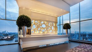 A modern reception area with a large window, a geometric patterned floor, and two potted plants. - Sortis Hotel, Spa & Casino, Autograph Collection by Marriott (Panama City)