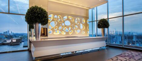A modern reception area with a large window, a geometric patterned floor, and two potted plants.