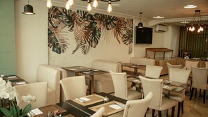A restaurant with a tropical leaf mural, multiple dining tables, and chairs. - Hôtel Belle Vue & Spa (Meknes)