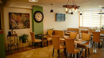 A dining area with multiple tables and chairs, a wall clock, and a large painting.