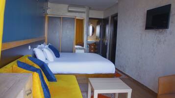 Ein Hotelzimmer mit einem großen Bett, einem Schreibtisch, einem Stuhl, einem Fernseher und einem durchgehenden Türspalt einsehbaren Badezimmer.