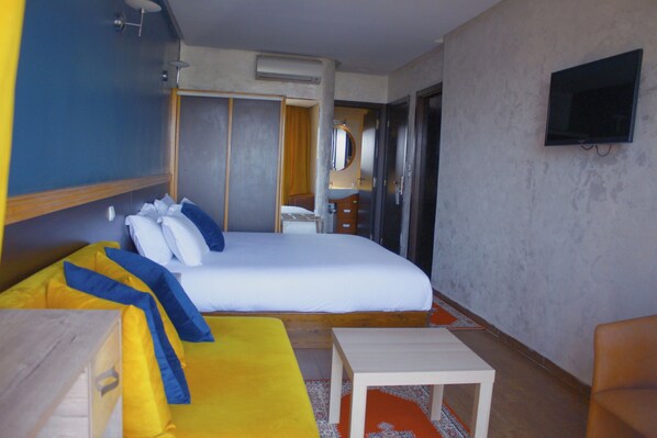 Habitación de hotel con una cama grande, un escritorio, una silla, un televisor y un baño visible a través de una puerta abierta.