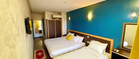 Habitación de hotel con dos camas, un tapete rojo, piso de madera, pared azul y un espejo.