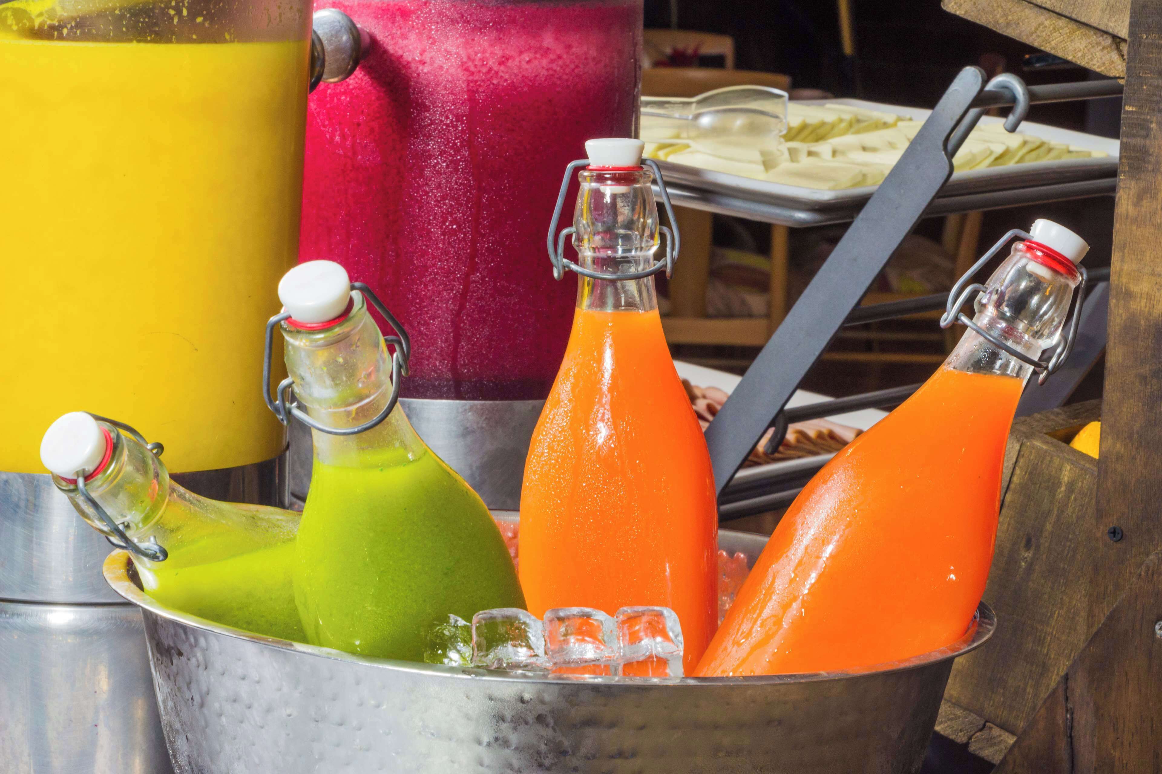 A metal container holding three bottles of juice with ice cubes.