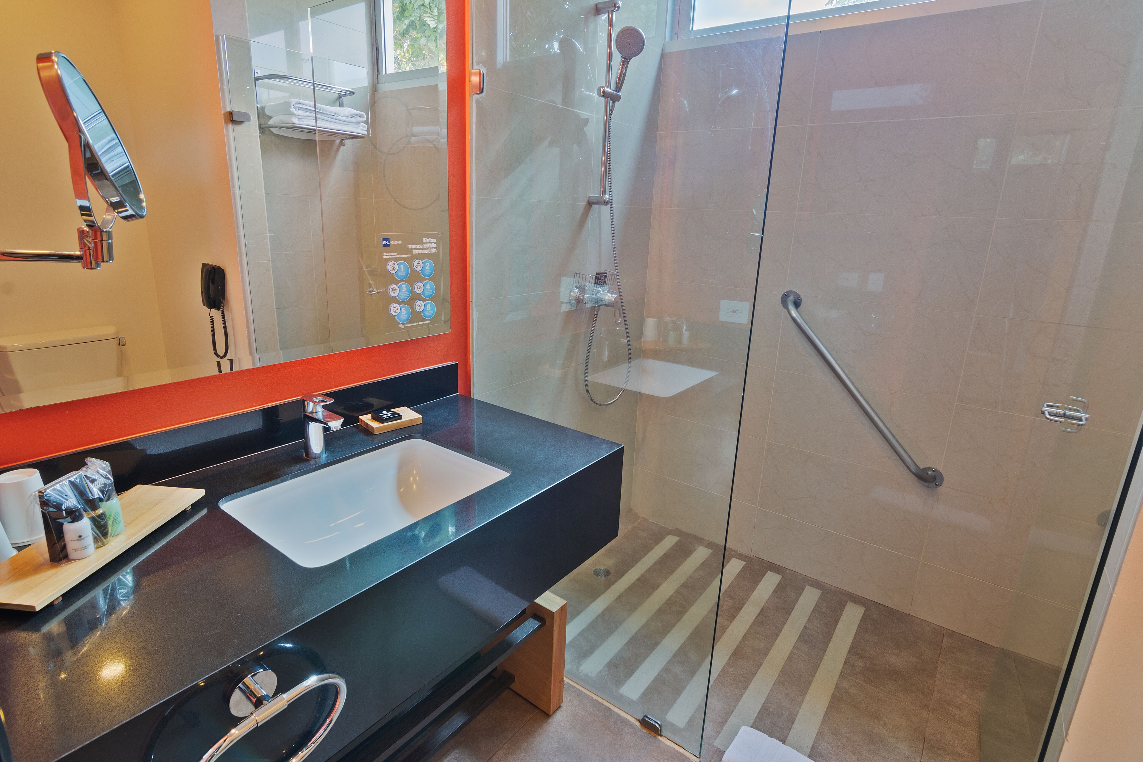 Un baño moderno con ducha envuelta en vidrio, encimera negra y un espejo grande.