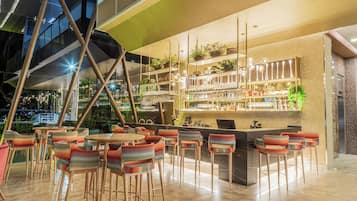 Zona de bar moderna con techo alto, taburetes y estantes llenos de botellas y vasos.