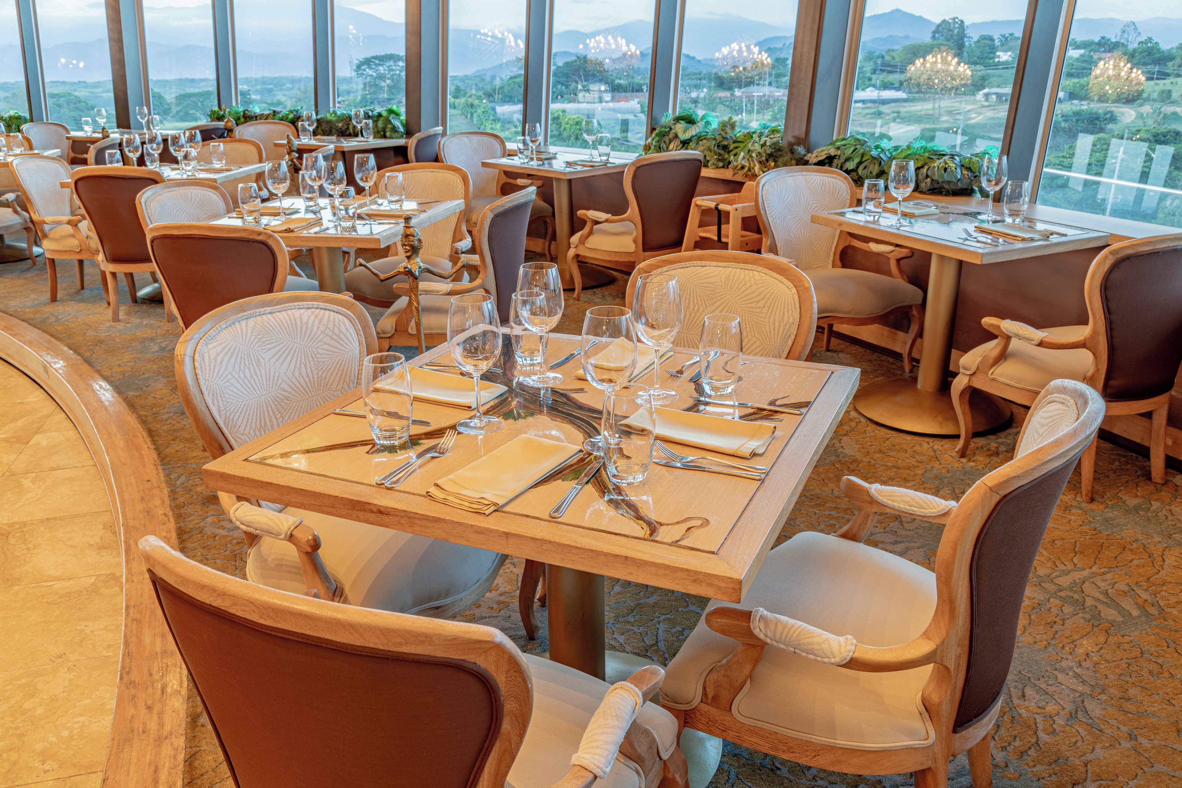 A restaurant with multiple tables set for dining, chairs, and a view of the outdoors.