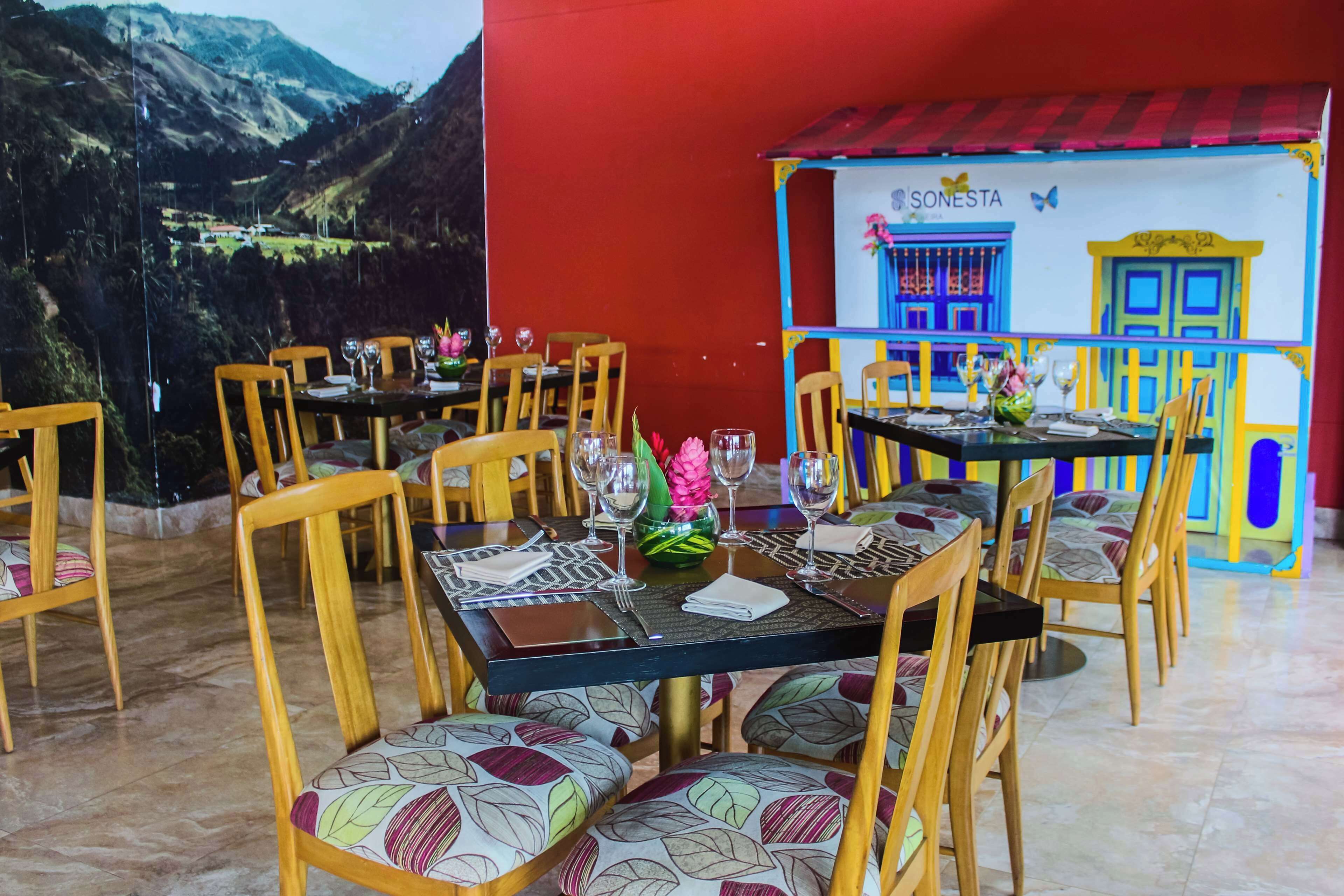 A restaurant with tables set for dining, chairs with patterned cushions, and a mural of a colorful building.