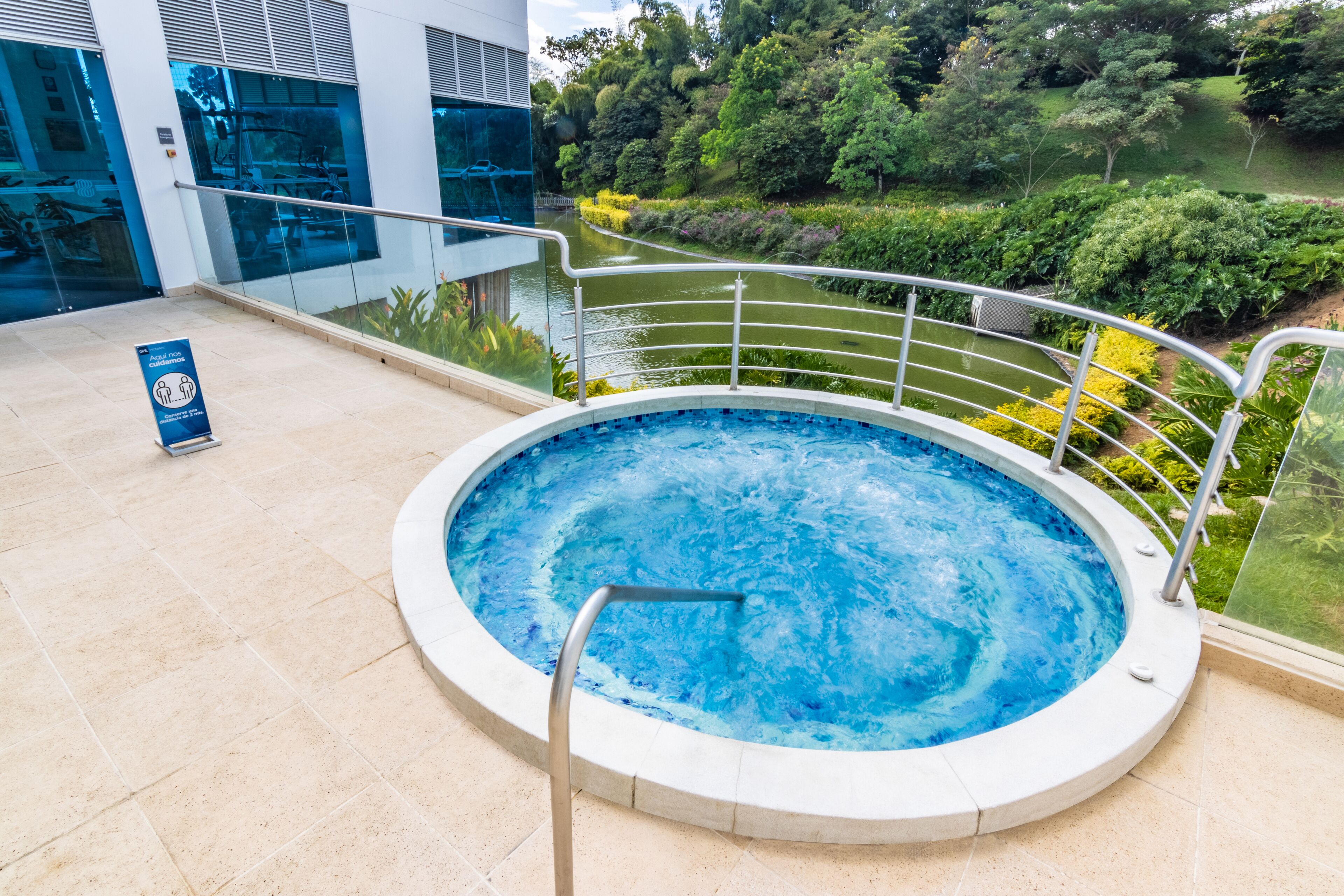 Un jacuzzi con baranda de metal, rodeado por un balaustrada de vidrio, con vistas a un jardín ajardinado y un edificio al fondo.