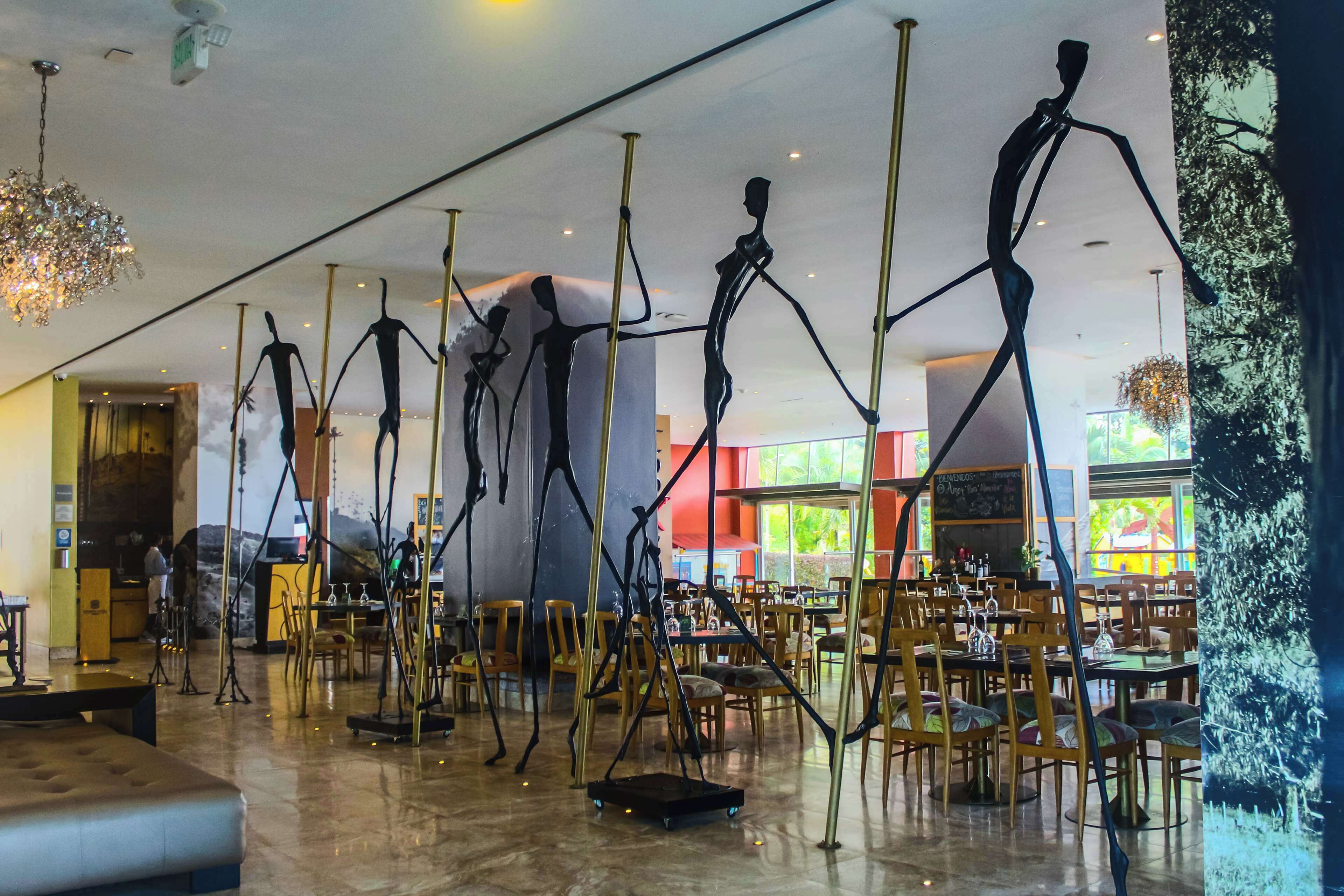 A spacious indoor area with multiple dining tables and chairs, a large chandelier, and abstract sculptures.