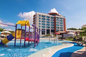Un espace de jeux aquatiques avec un toboggan et une structure d’escalade, entouré d’une piscine agrémentée de chaises longues et de parasols.