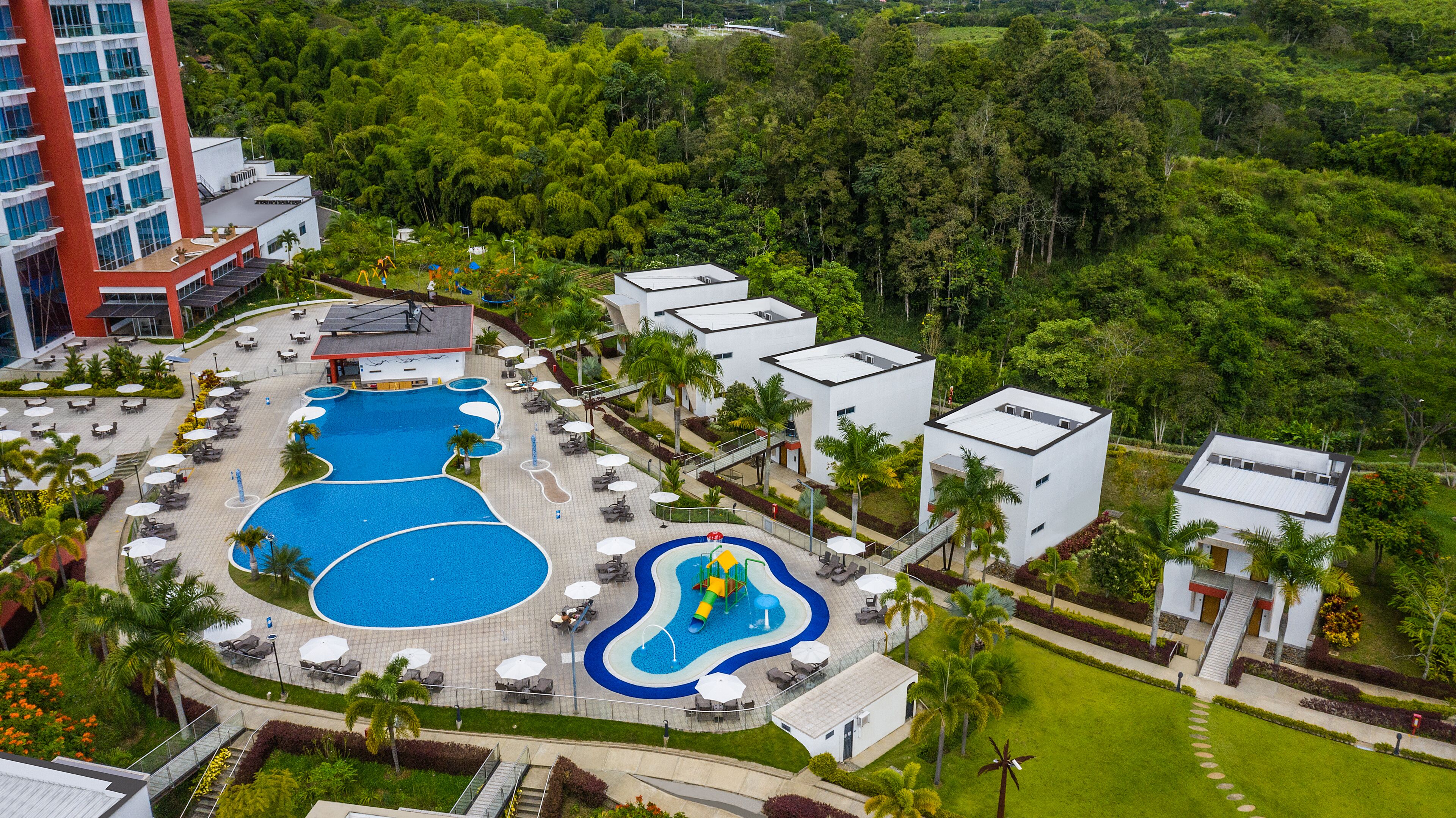 Un resort con una amplia piscina, zona de juegos infantiles y varios edificios con balcones.