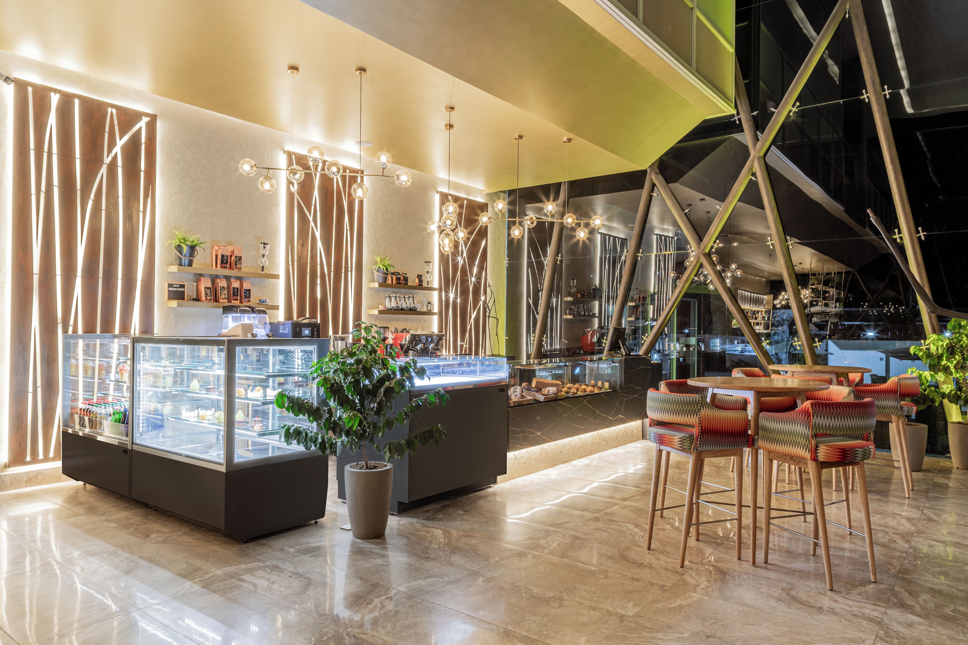 L’intérieur d’un café moderne se caractérise par un sol en marbre, un présentoir central où sont exposées des pâtisseries, et un espace salon avec des chaises aux couleurs vives.