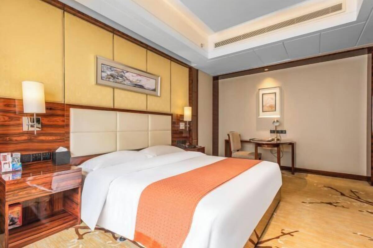 A hotel room with a large bed, a wooden nightstand, a desk, and a chair.
