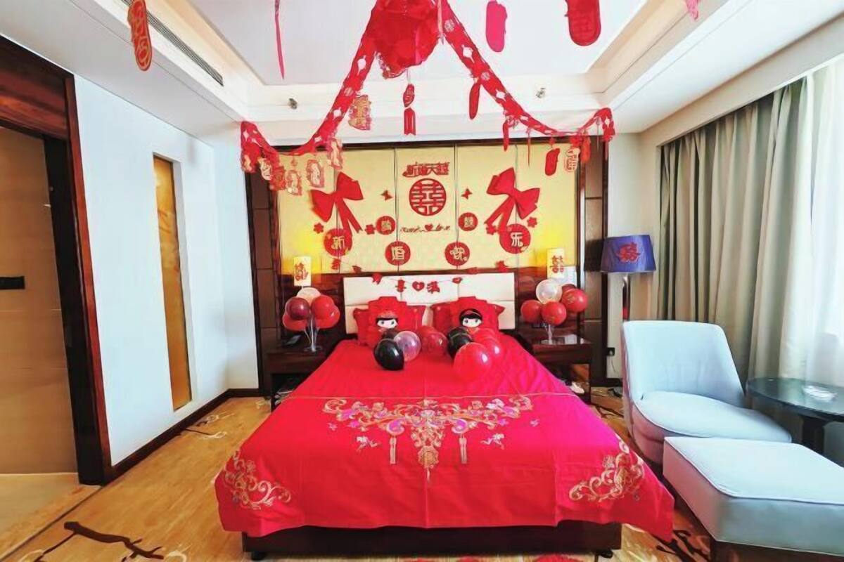 A hotel room with a red bedspread, a wooden headboard, and red decorations.