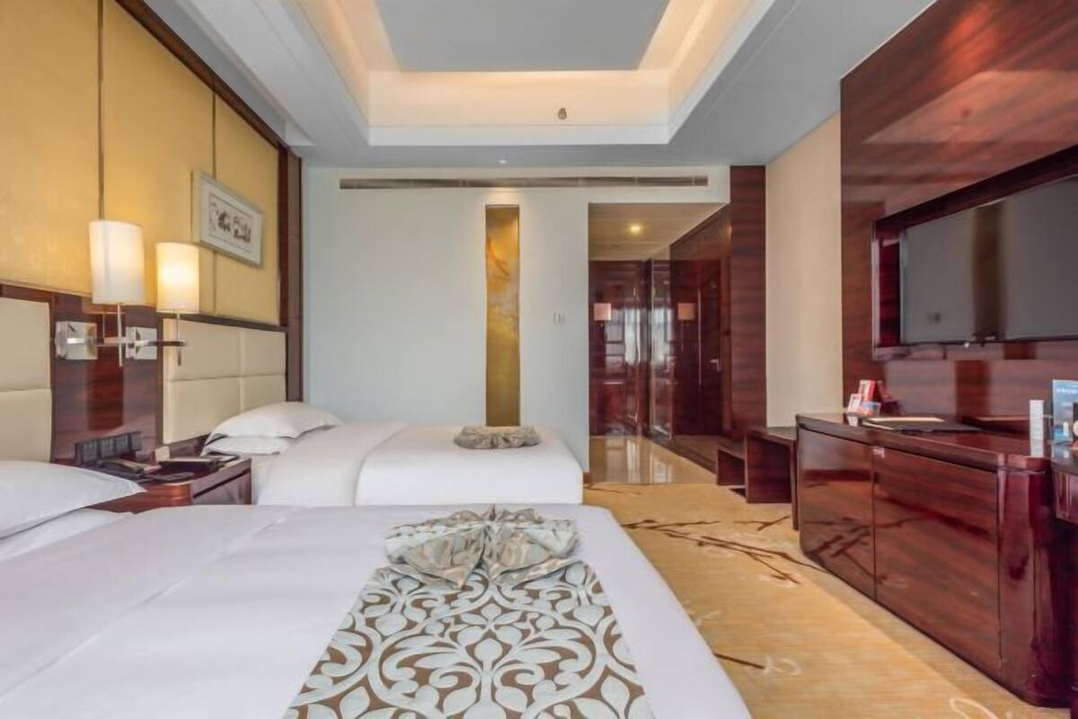 A hotel room with two beds, a large mirror, a wooden dresser, and a flat-screen TV.
