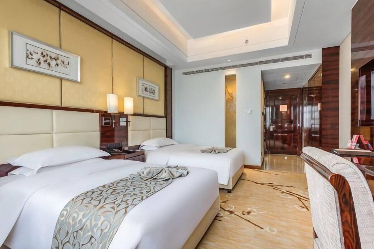 A hotel room with two beds, a sitting area, and a bathroom visible through an open door.