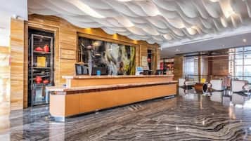 A hotel lobby with a reception desk, seating area, and a large window.