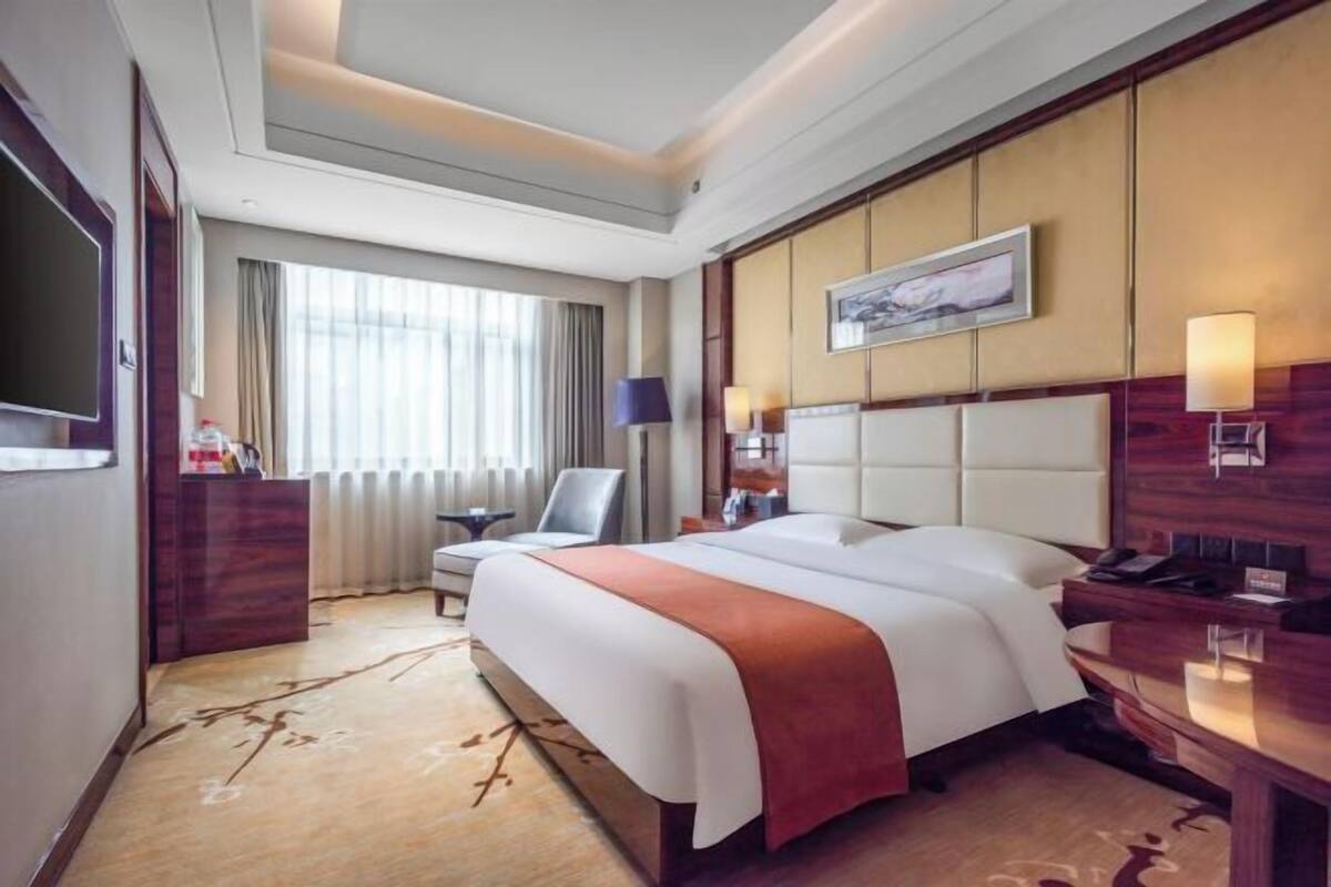 A hotel room with a large bed, a desk, a chair, a TV, and a window with curtains.