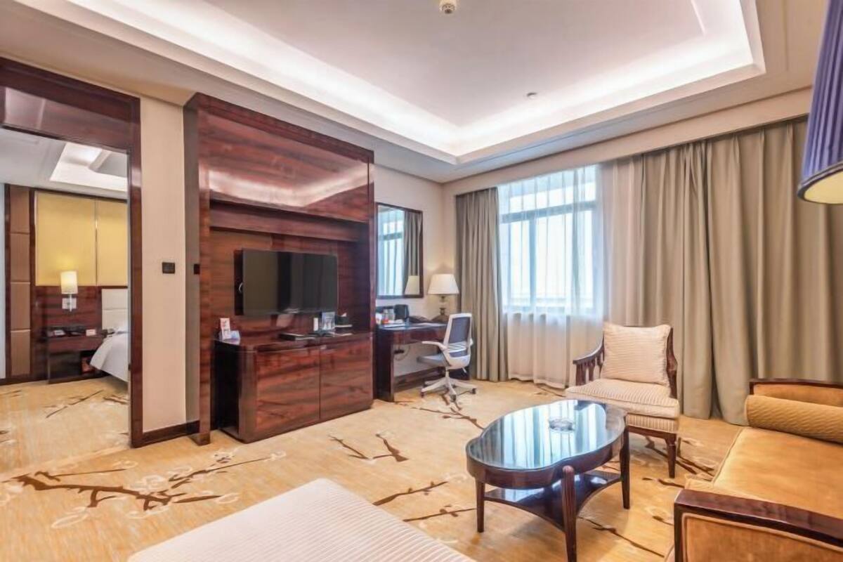 A hotel room with a wooden accent wall, a flat-screen TV, a desk with a chair, a round coffee table, and a sofa.
