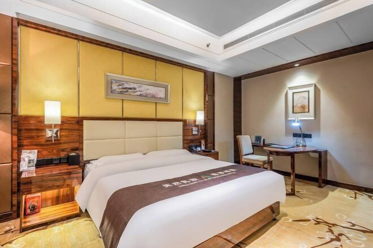 A hotel room with a large bed, a desk, a chair, and a wall-mounted TV.