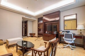 A hotel room with a round dining table, wooden chairs, a sofa, a desk with a computer, a TV, and a mirror. - Prestton Hotel (Jinan)