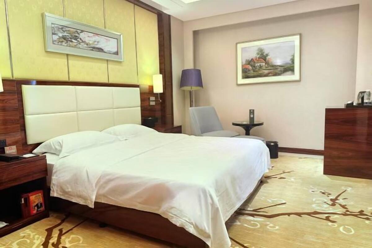 A hotel room with a large bed, a nightstand, a lamp, and a chair.