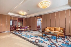 A spacious lobby with a large sofa, a coffee table, and a dining area with chairs and a table. - Prestton Hotel (Jinan)