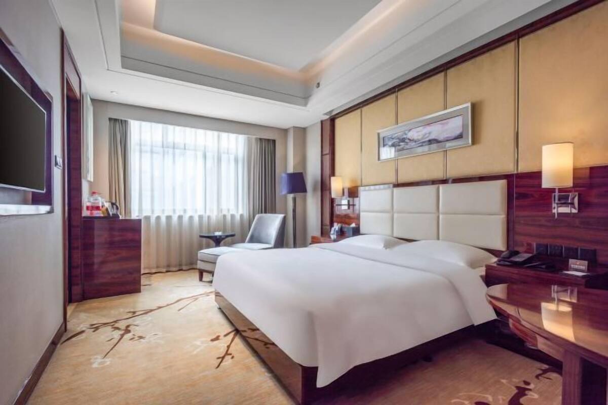 A hotel room with a large bed, a desk, a chair, a TV, and a window with curtains.