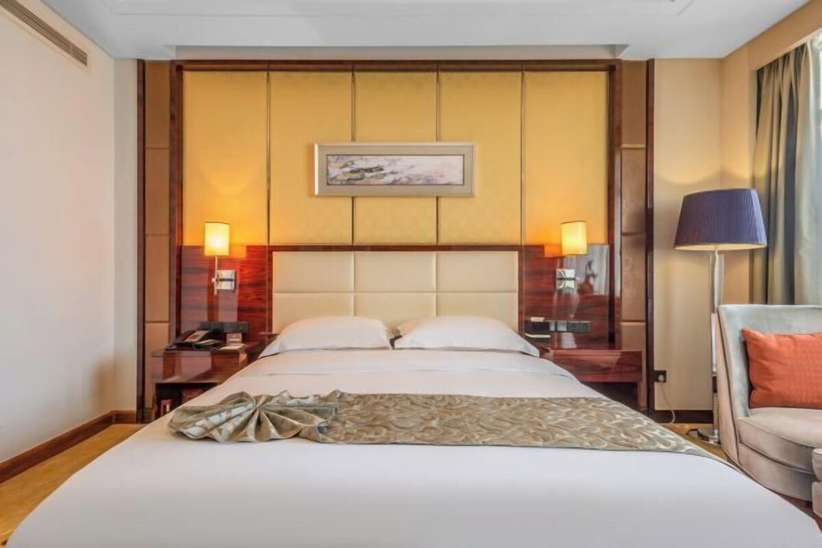 A hotel room with a large bed, two bedside tables with lamps, a chair, and a painting on the wall.