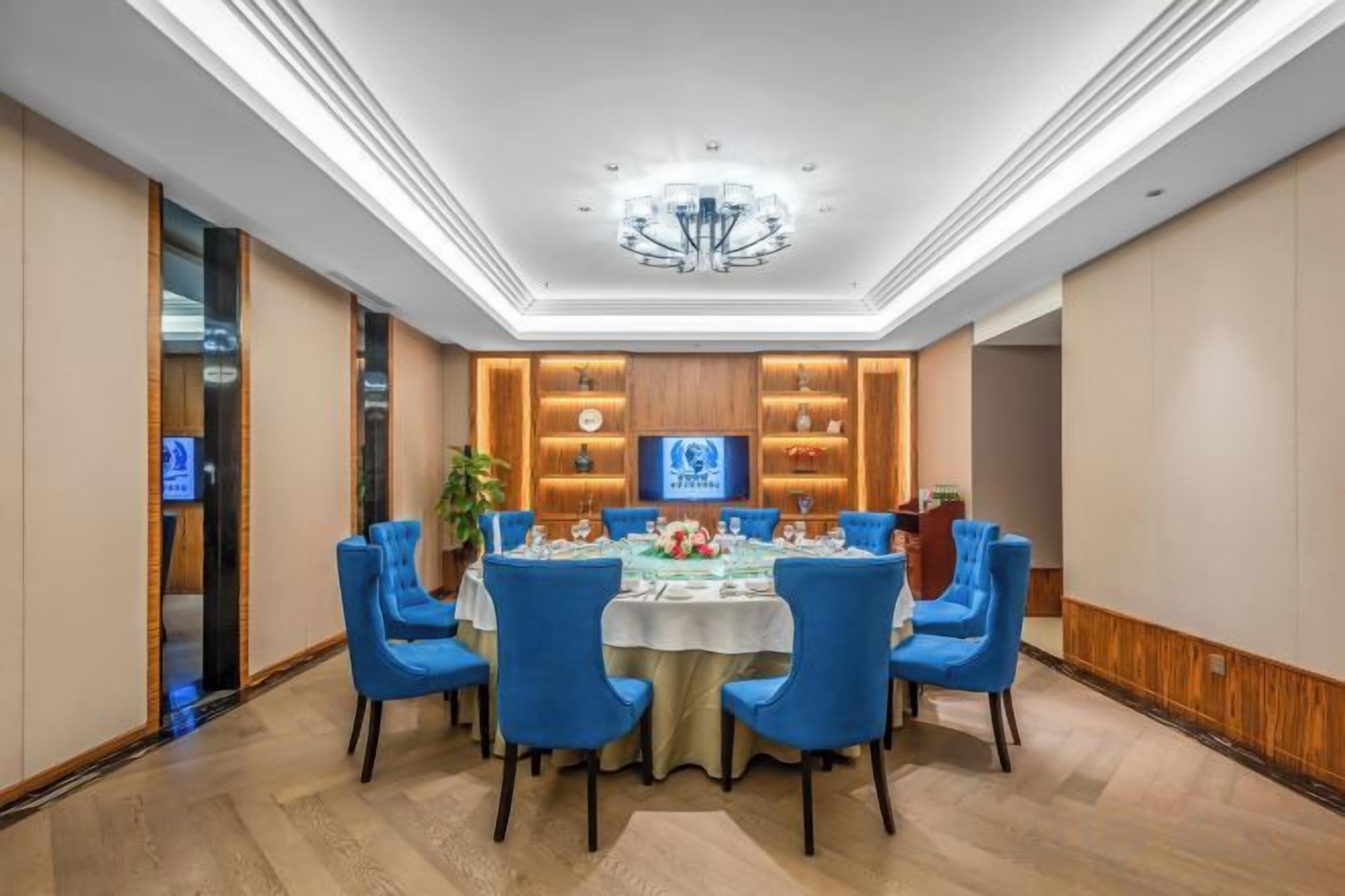 A conference room with a round table, blue chairs, and a chandelier.