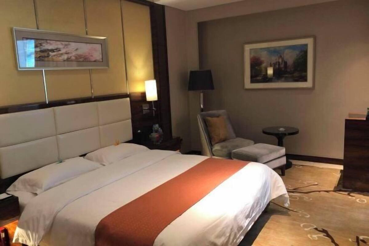 A hotel room with a large bed, a chair, a small table, and artwork on the walls.