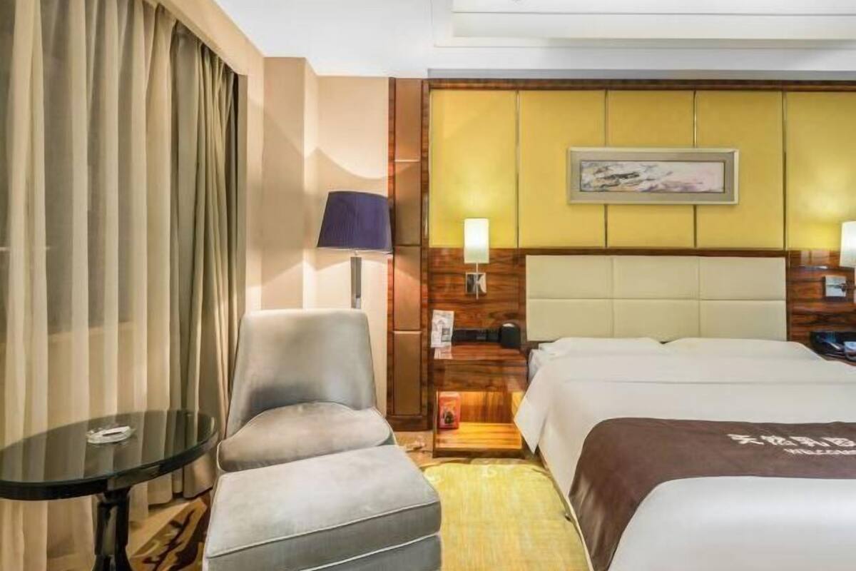 A hotel room with a bed, a seating area with a table, a lamp, and a wall-mounted artwork.