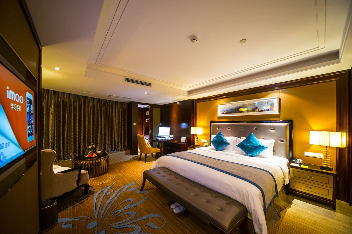 Une chambre d’hôtel avec un grand lit, un bureau, une chaise, une télévision et un écran de télévision affichant le site web de l’hôtel.