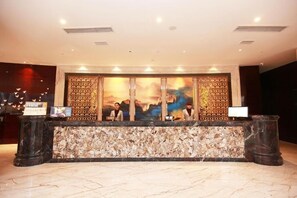 A reception desk with a marble counter, two receptionists, and a large decorative wall with a cityscape painting.