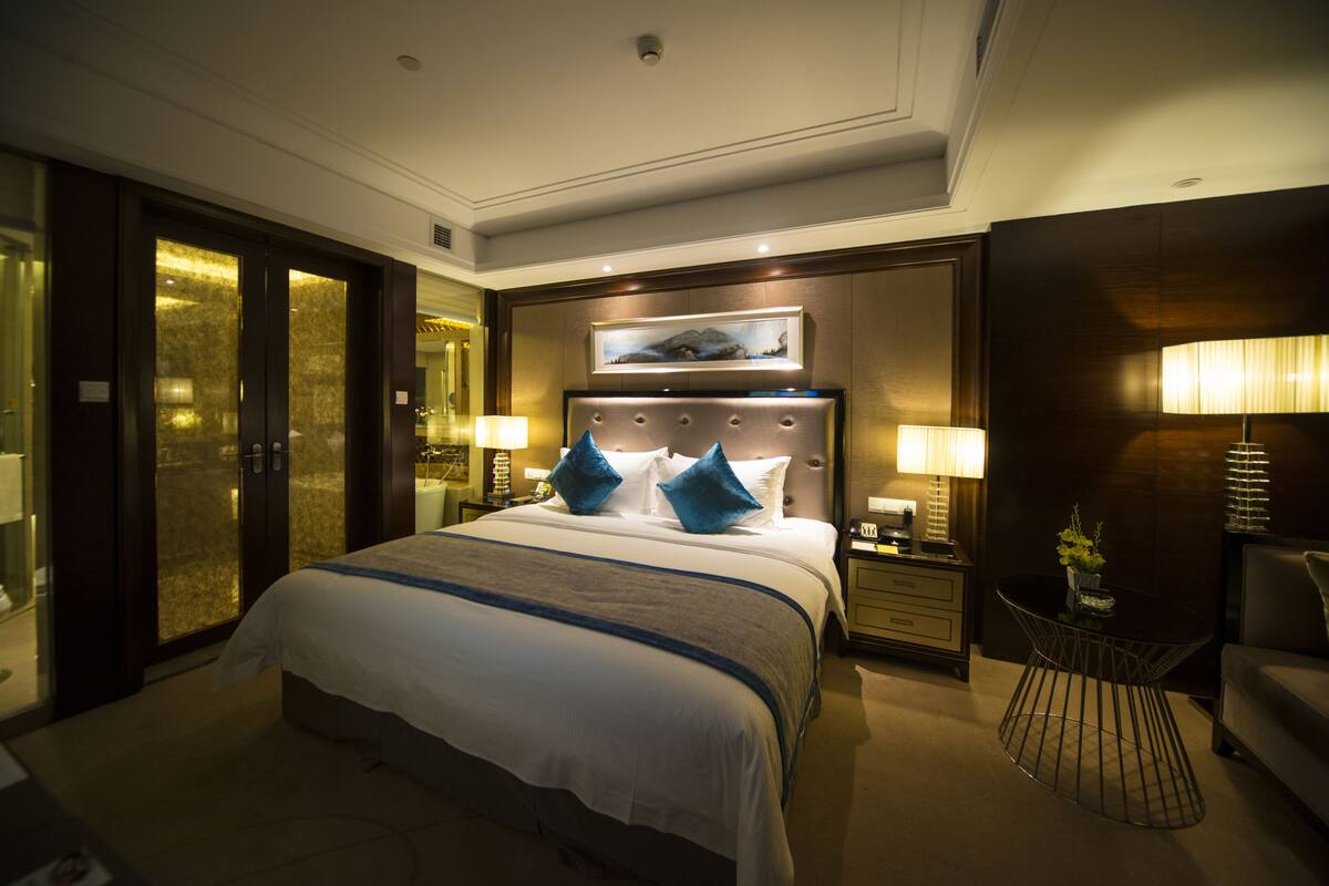 Une chambre d’hôtel avec un grand lit, une table de chevet avec une lampe, une petite table avec une plante et une chaise.