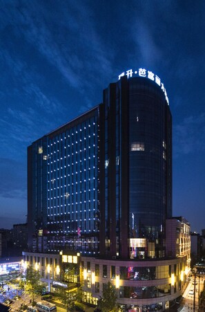 A modern hotel with a curved facade, illuminated windows, and a prominent sign at the top.