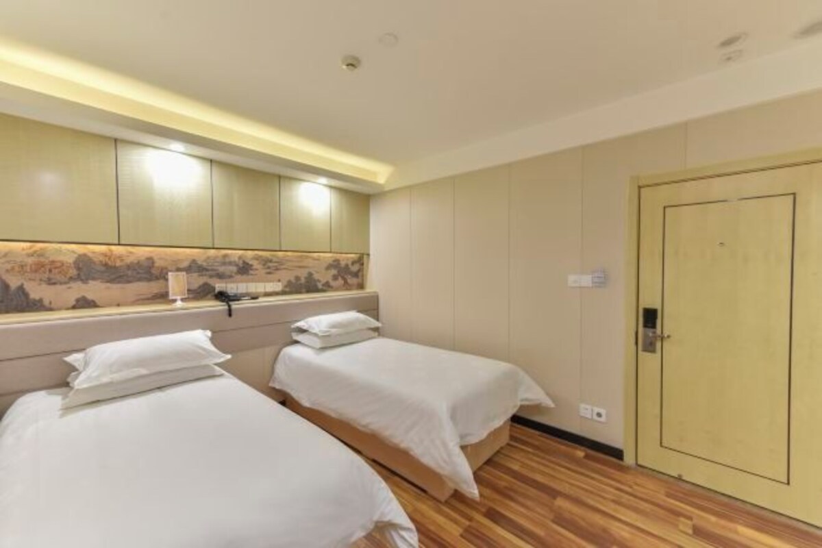 Een hotelkamer met twee eenpersoonsbedden, een houten vloer, een grote spiegel en een deur.