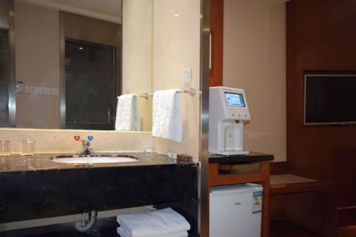 Een hotelbadkamer met een wastafel, spiegel, handdoekhouder en een kleine koelkast.