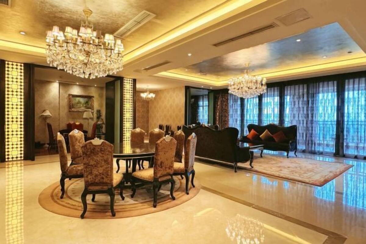 A spacious dining area with a round table and chairs, a chandelier, and a sofa in the background.